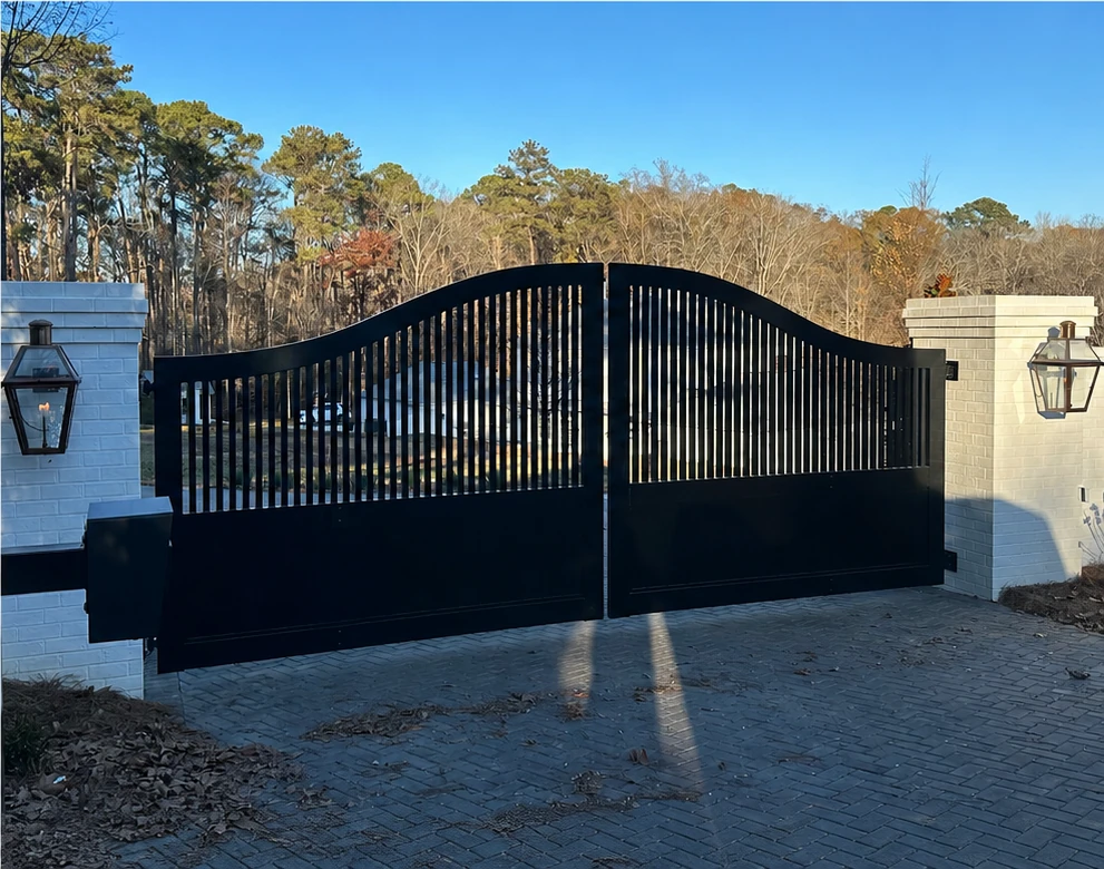 Black ornamental driveway gate between brick columns at a Birmingham home